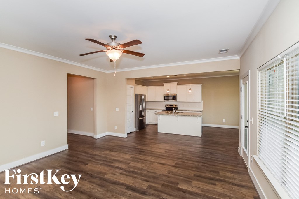 an empty living room with a ceiling fan and a kitchen