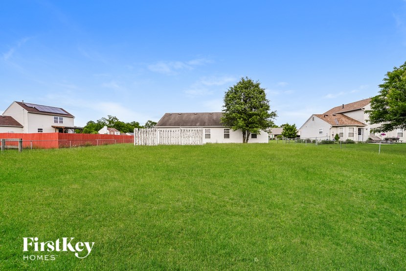 A grassy field with a white house and a tree in the distance.