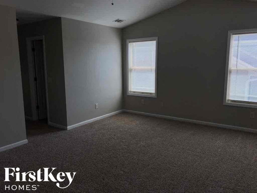 A room with a carpeted floor and two windows.