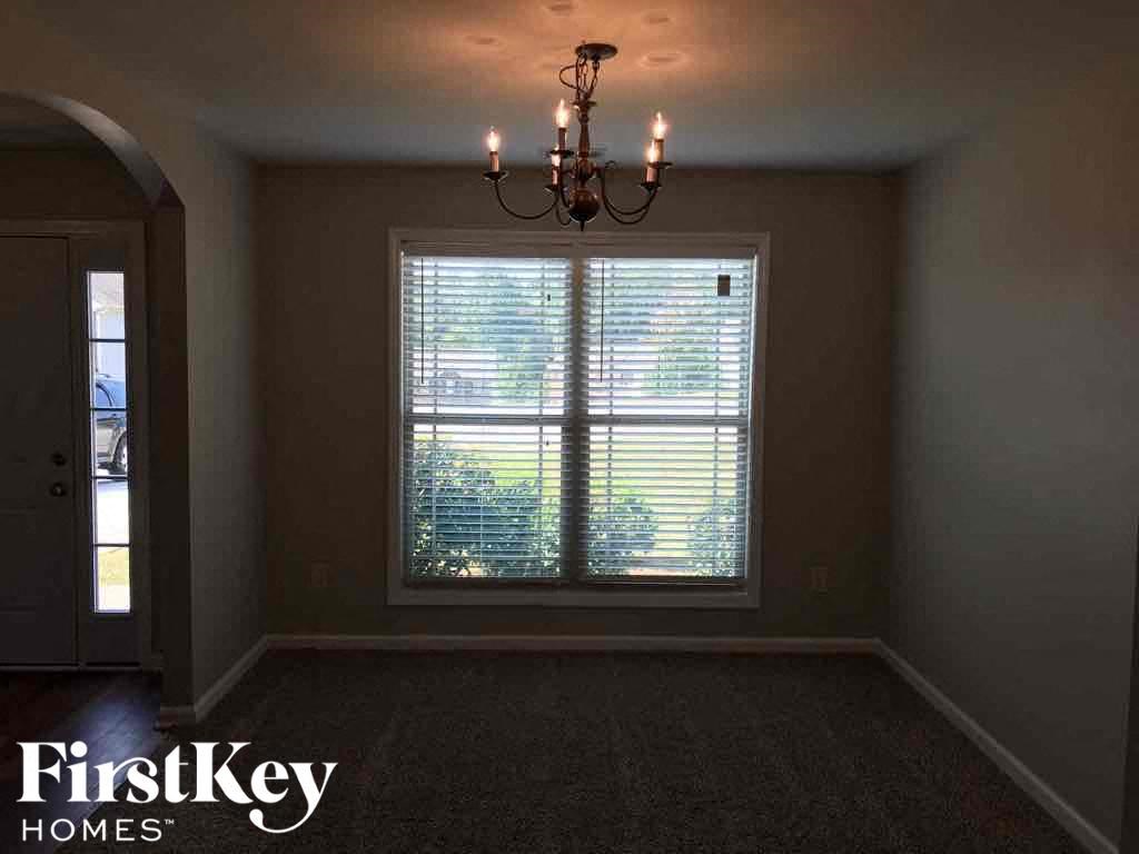 A room with a chandelier, a window with blinds, and a door.