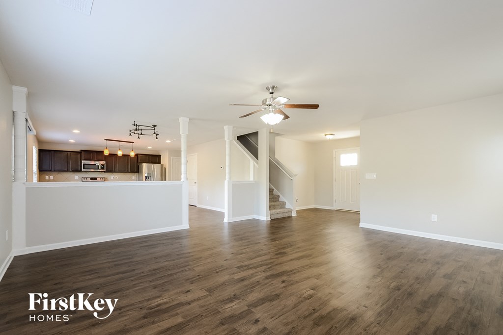 an empty living room with a ceiling fan and a kitchen