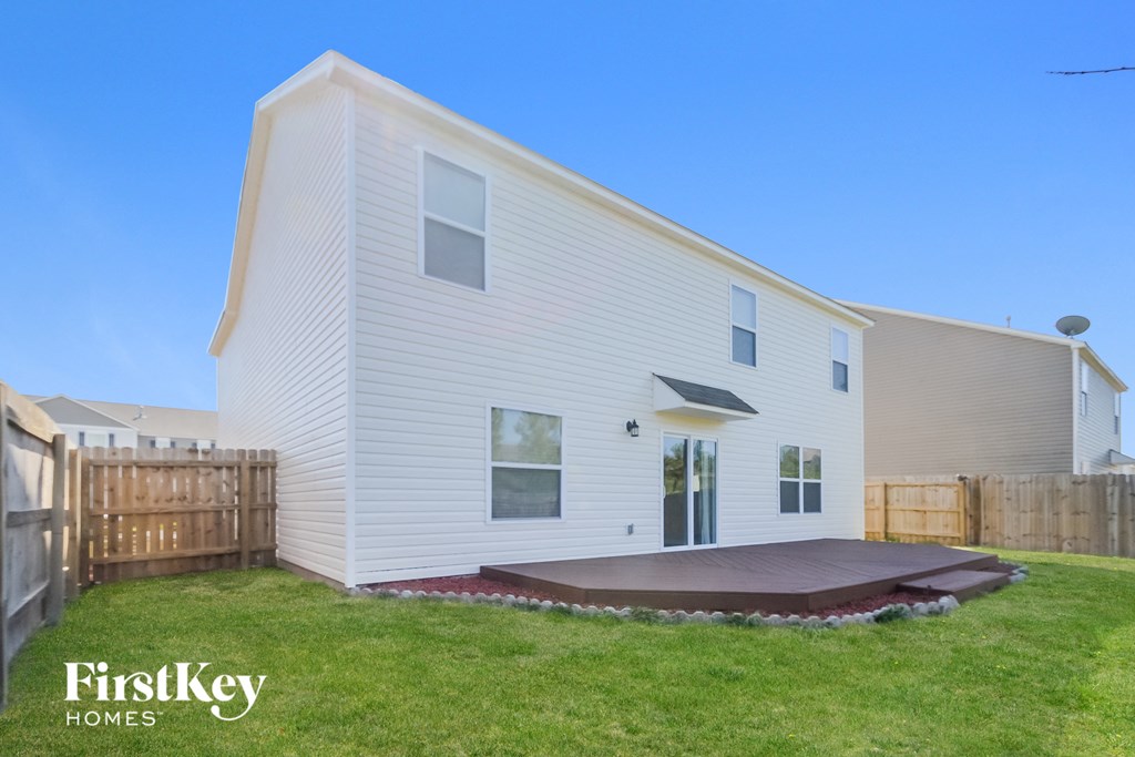 the back of a white house with a yard and a wooden fence