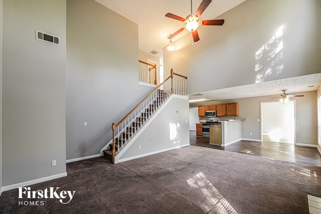A spacious living room with a staircase and a ceiling fan.
