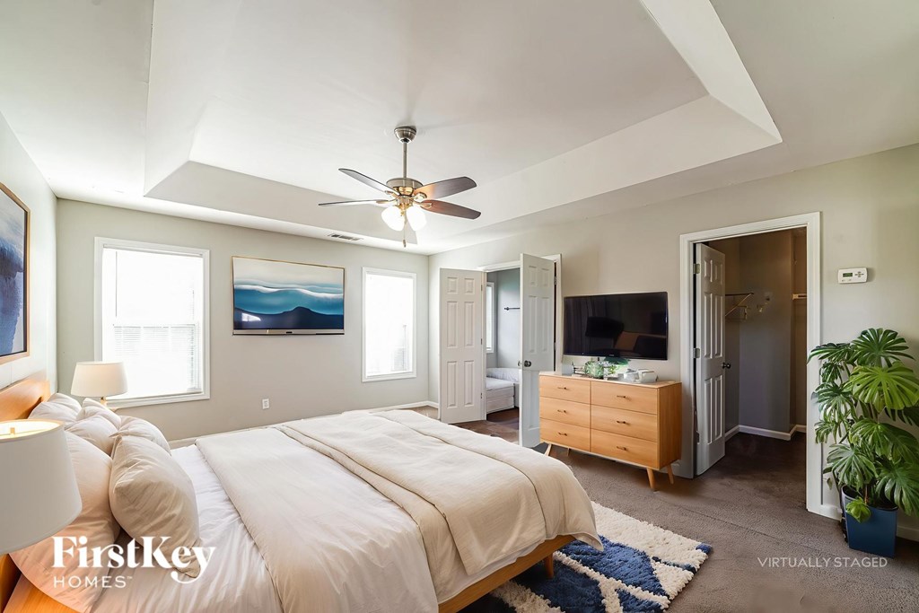 A bedroom with a large bed, a ceiling fan, and a television.