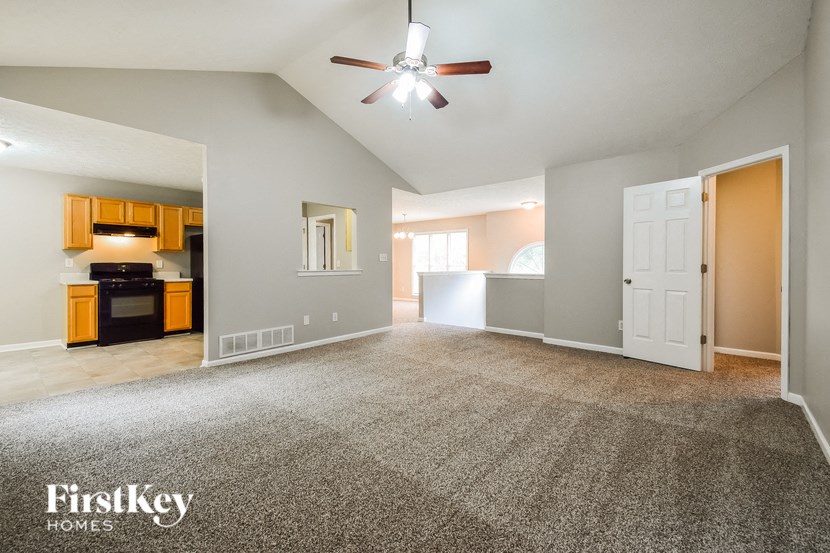 an empty living room with a ceiling fan and a kitchen