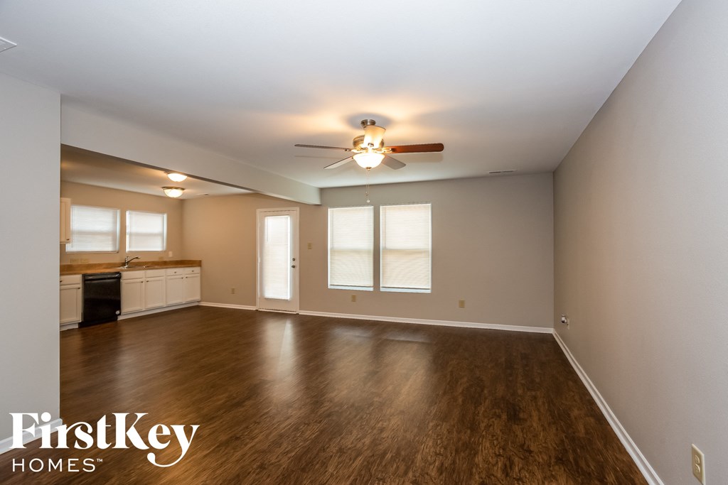 an empty living room with a ceiling fan and a kitchen