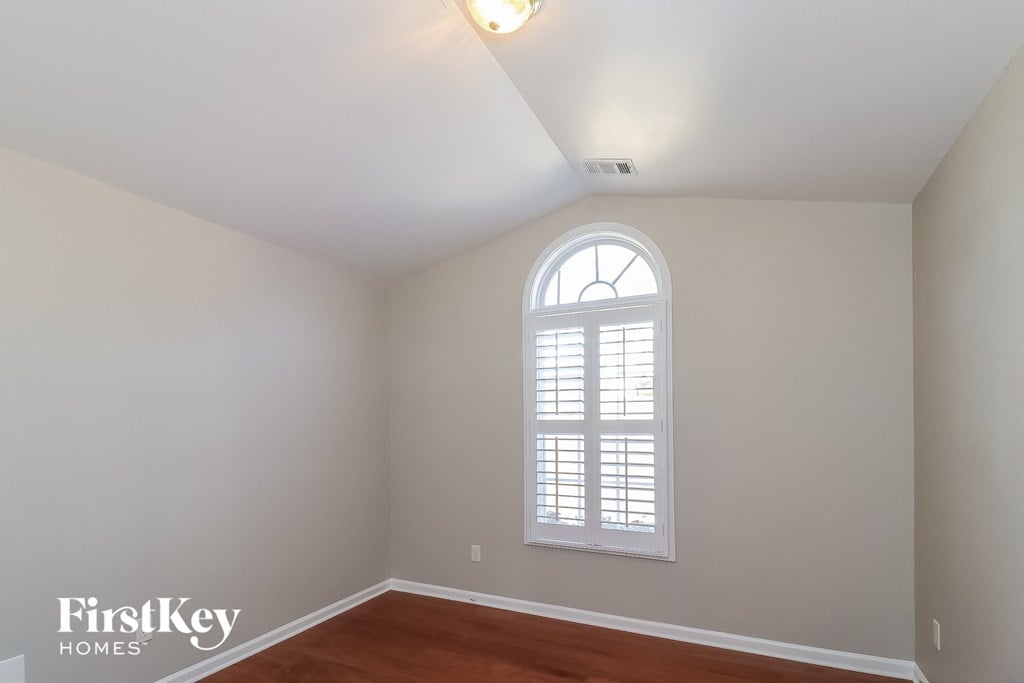 the second bedroom has a large arched window and hardwood floors