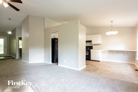 A spacious living room with a ceiling fan and a kitchen area in the background.