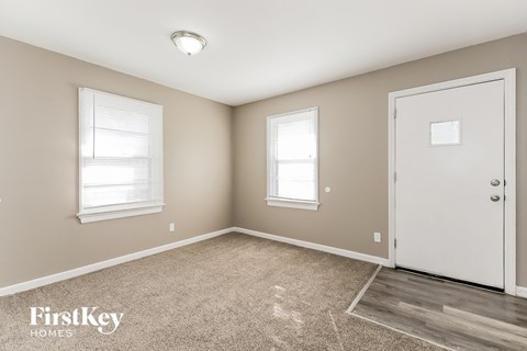 A room with a carpeted floor, a door, and two windows.