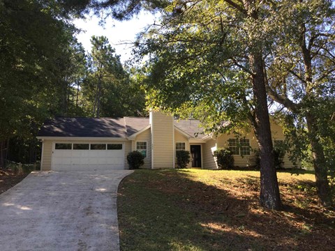 a yellow house with a driveway and trees