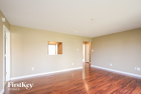 A room with wooden floors and a window is empty and waiting to be furnished.