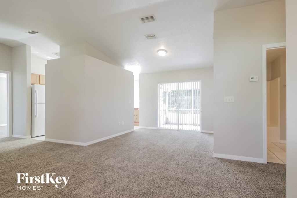 A spacious, empty room with a carpeted floor and a window with blinds.