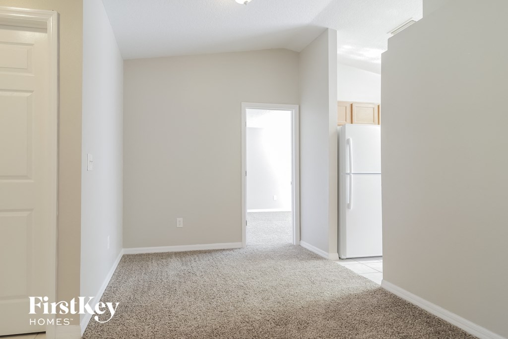 A carpeted room with a door on the left and a refrigerator on the right.