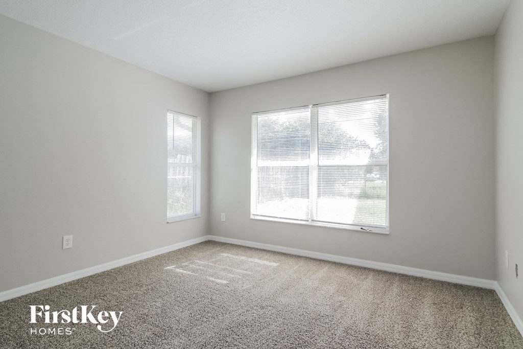 A room with a carpet floor and two windows.