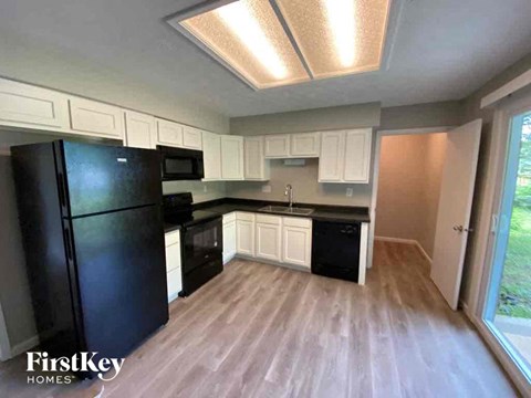 an empty kitchen with a black refrigerator and white cabinets