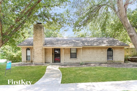 the front of a brick house with a sidewalk and a tree