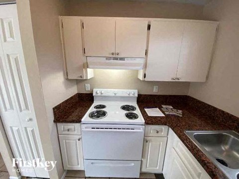 A kitchen with a white stove top oven and white cabinets.