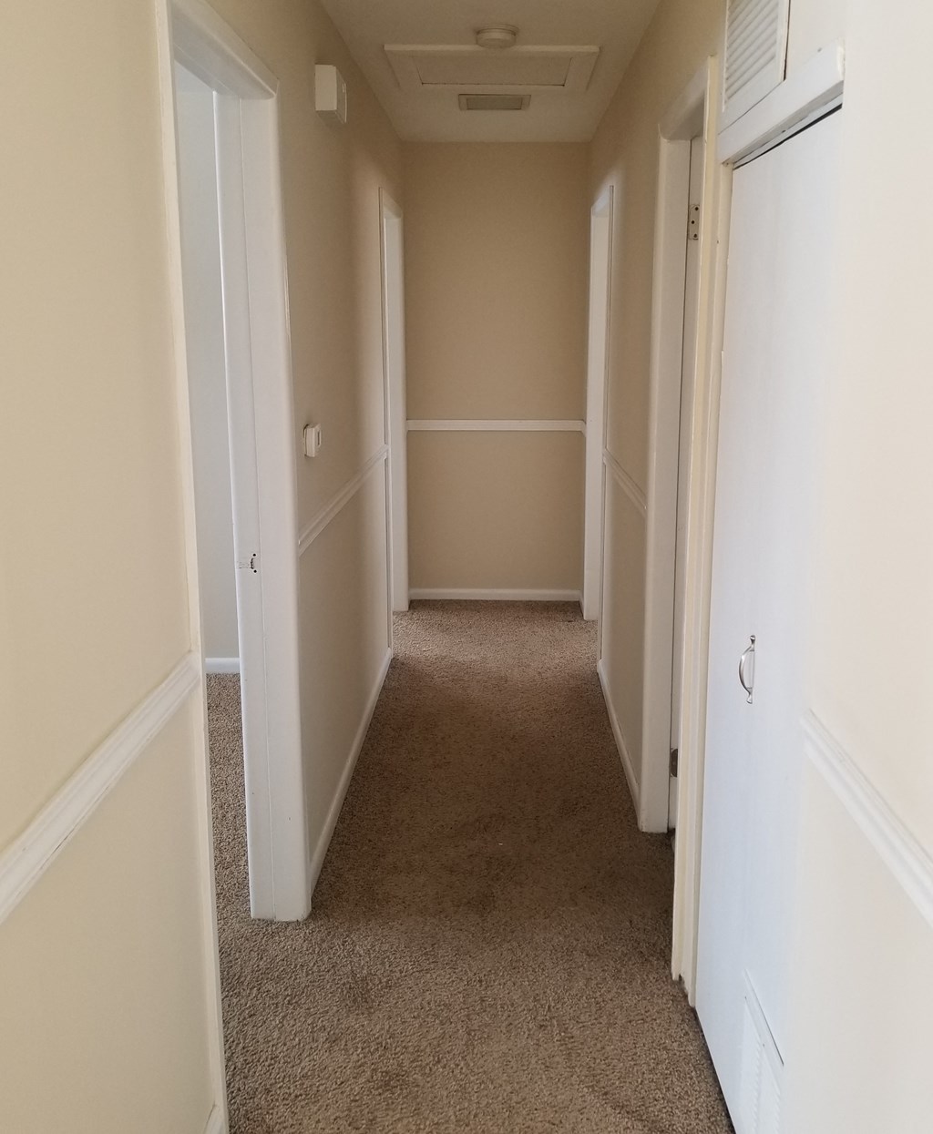 a hallway with a carpeted floor and beige walls and white doors