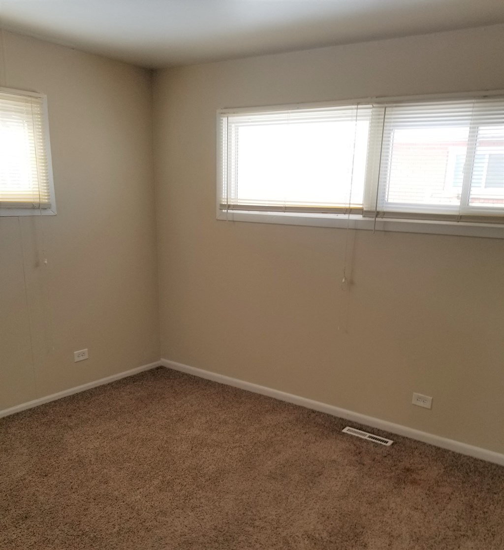 an empty room with two windows and a carpet