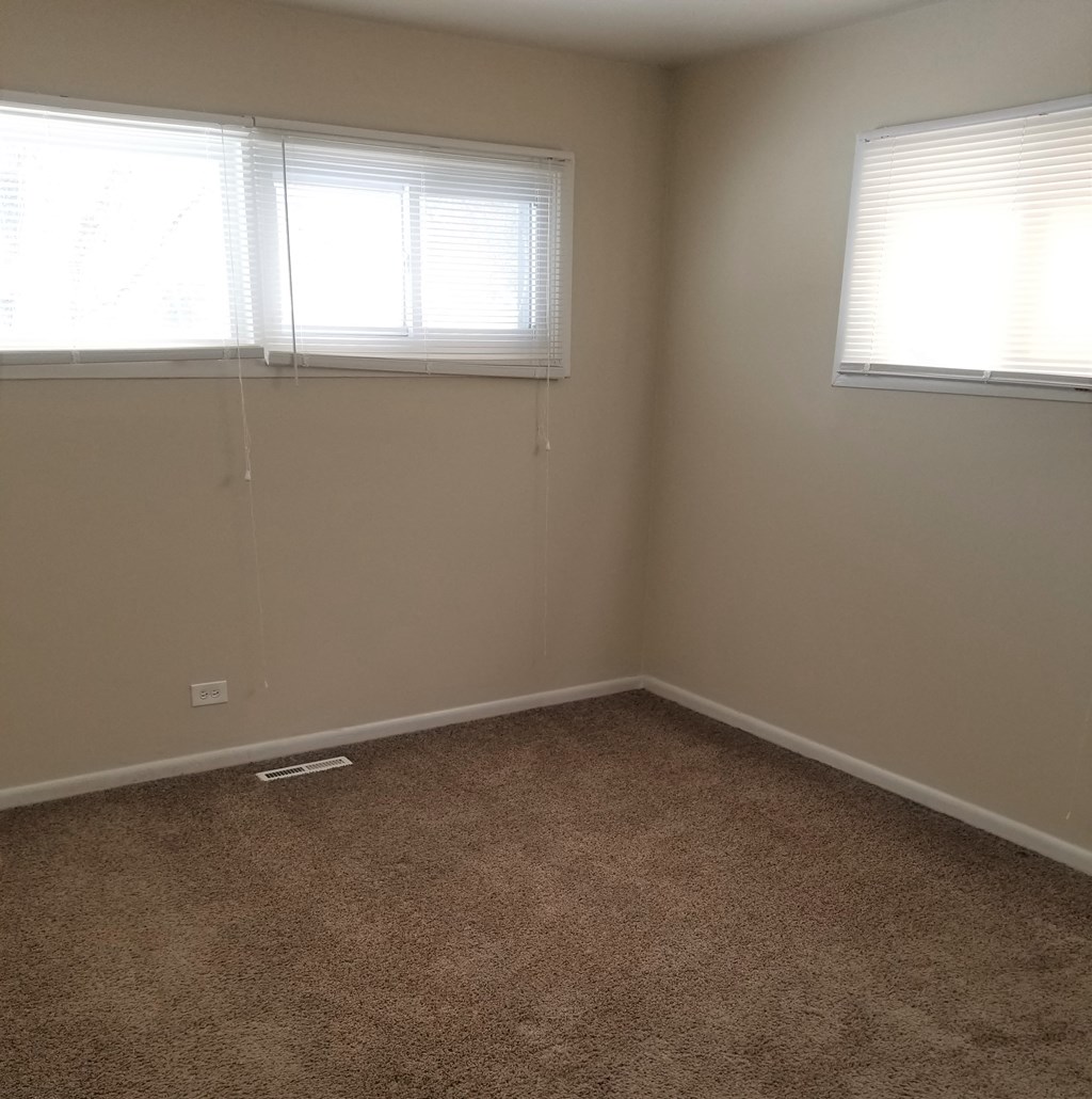 an empty room with two windows and a carpet