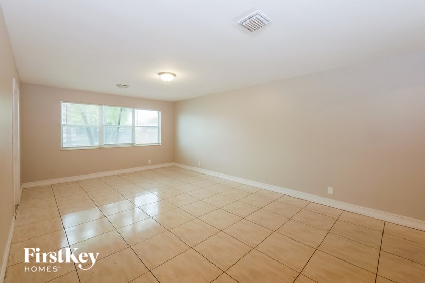 A spacious room with beige tiled flooring and a window letting in natural light.