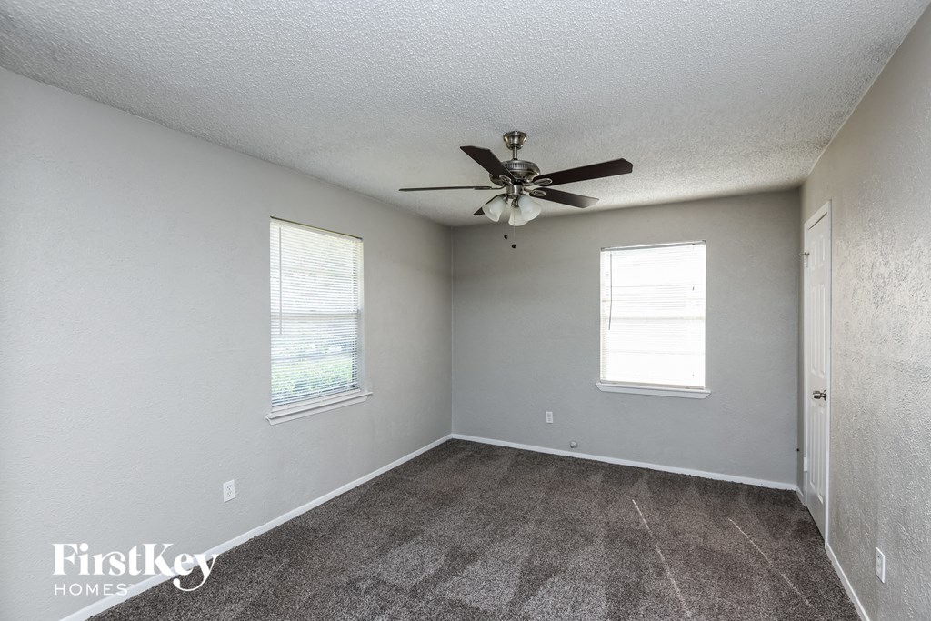 an empty room with a ceiling fan and two windows