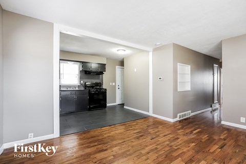 a renovated living room and kitchen with wood flooring and a black refrigerator and stove