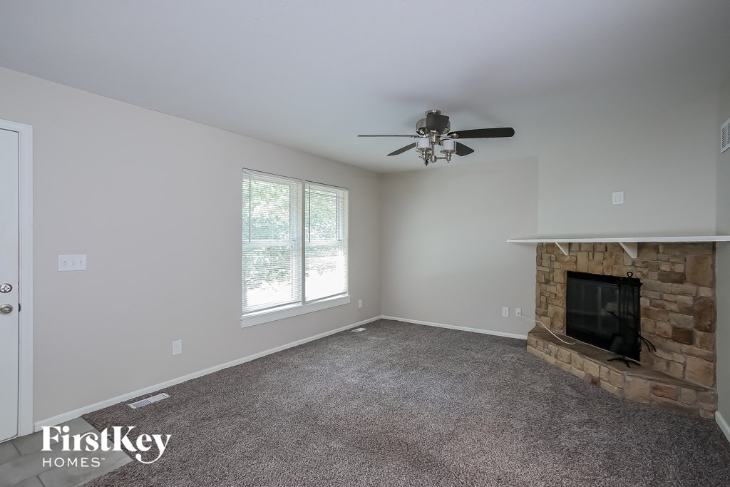the living room has a stone fireplace and a ceiling fan