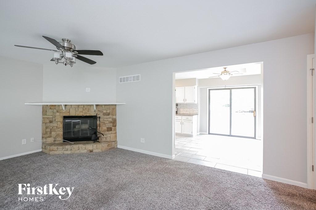 a living room with a stone fireplace and a ceiling fan