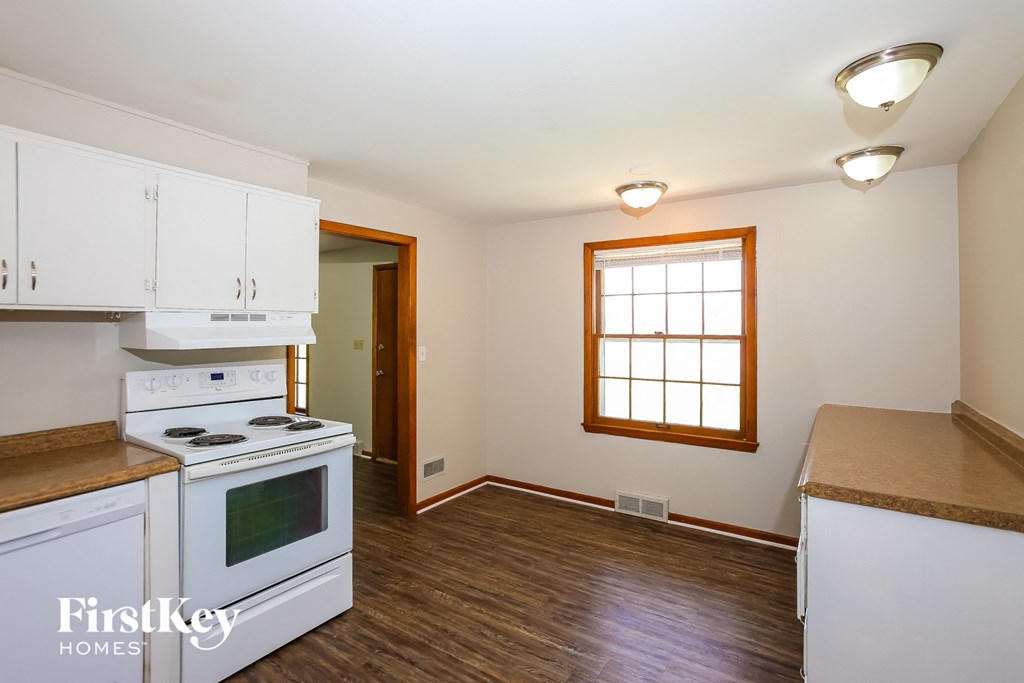 an empty kitchen with white appliances and white cabinets and a window