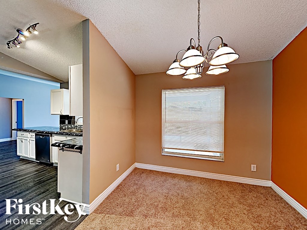 an empty dining room with a window and a kitchen