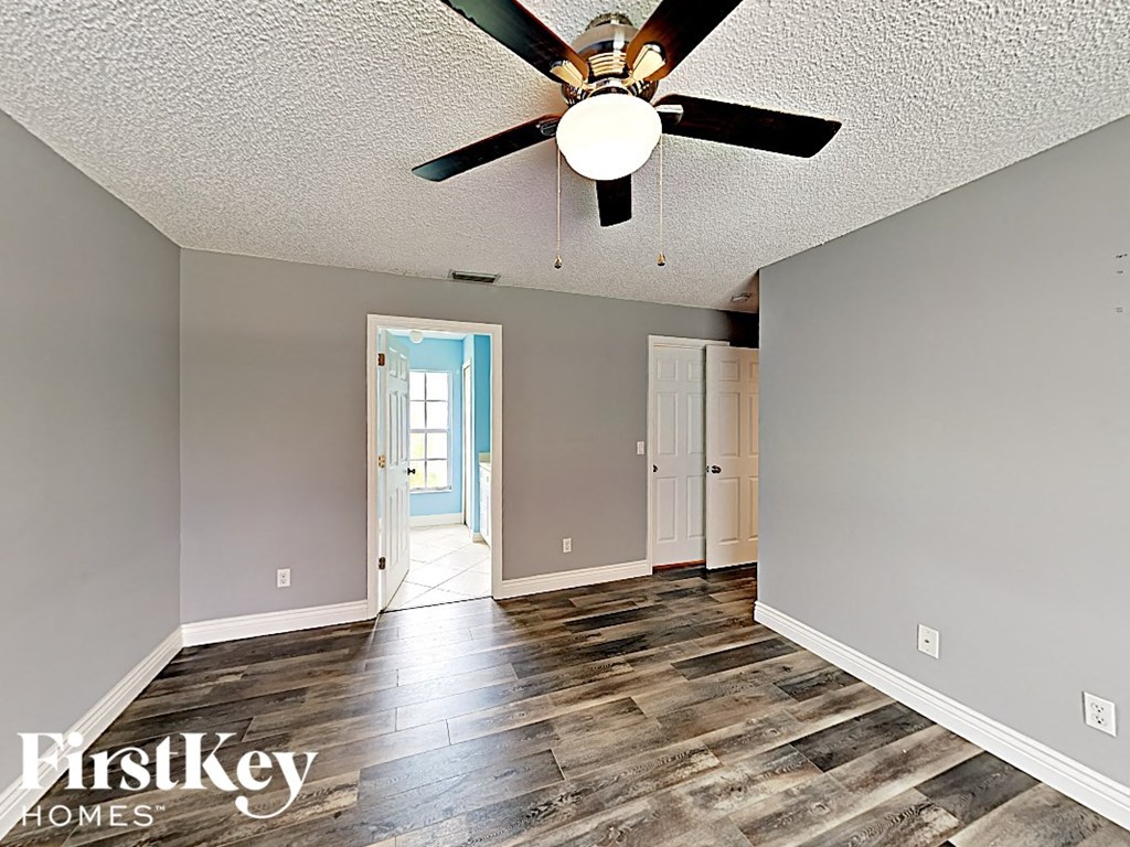 an empty living room with a ceiling fan and a door to a hallway