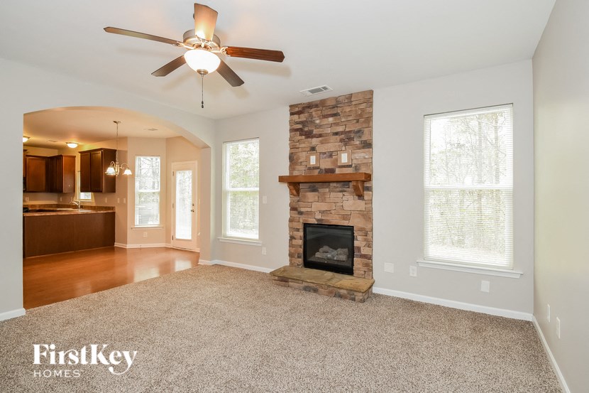 an empty living room with a stone fireplace and a ceiling fan