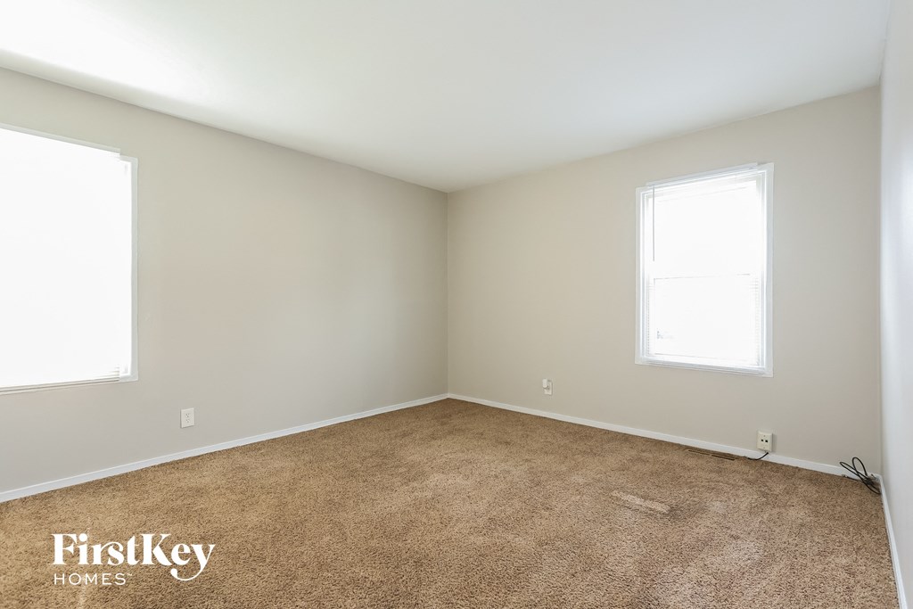 A room with a carpeted floor and two windows.