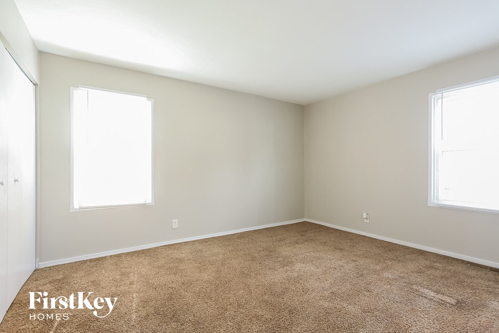 A room with a carpeted floor and two windows.