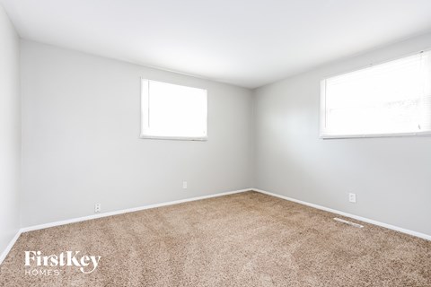 A room with a carpeted floor and two windows.