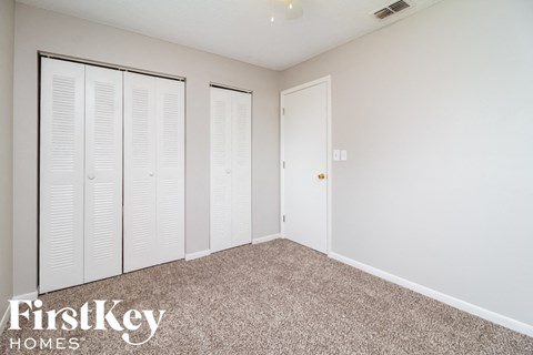 A bedroom with white closet doors and a carpeted floor.