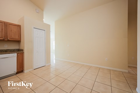 A spacious room with beige walls and tiled flooring, featuring a kitchen area with wooden cabinets and a white dishwasher.