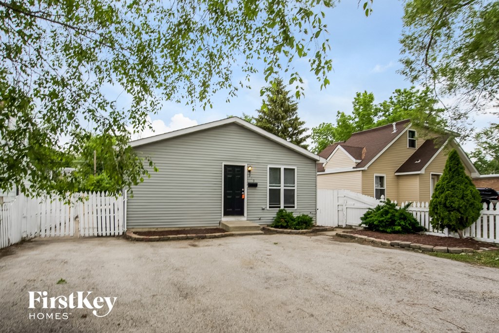 A house with a garage is surrounded by a white picket fence.
