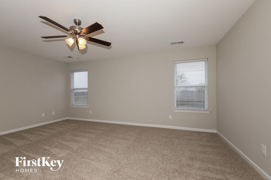a empty living room with a ceiling fan and two windows