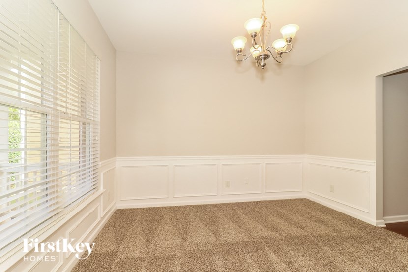 A room with a chandelier, a window with blinds, and a carpeted floor.