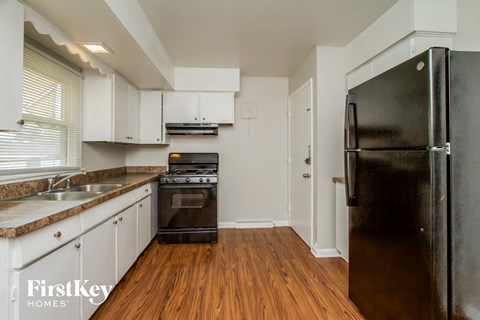 a kitchen with white cabinets and black appliances and a wooden floor