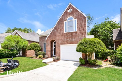 A brick house with a white garage door and a tree in front.