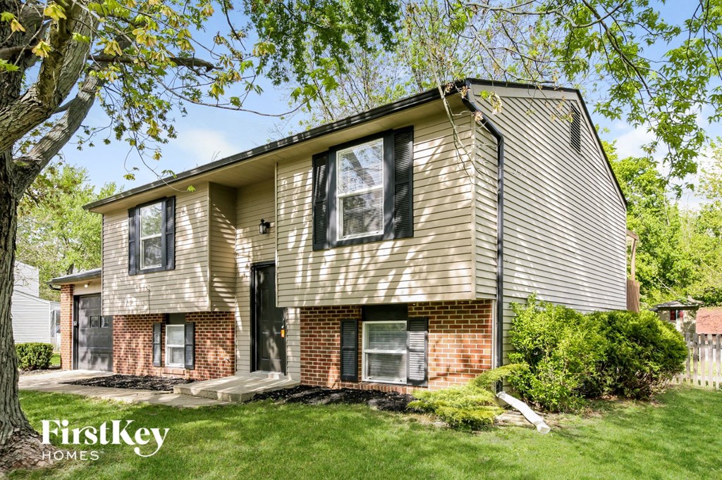 front view of a tan and brown house with trees and grass
