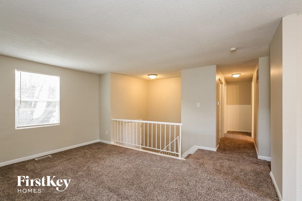 the living room and hallway of an empty home with carpeted floors and a staircase