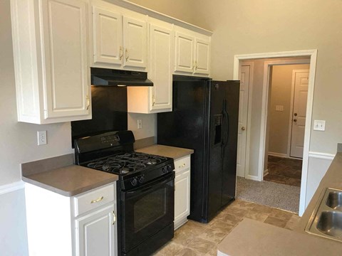 A black refrigerator sits in a kitchen with white cabinets.