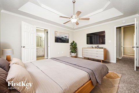 A bedroom with a large bed, a ceiling fan, and a dresser with a mirror above it.