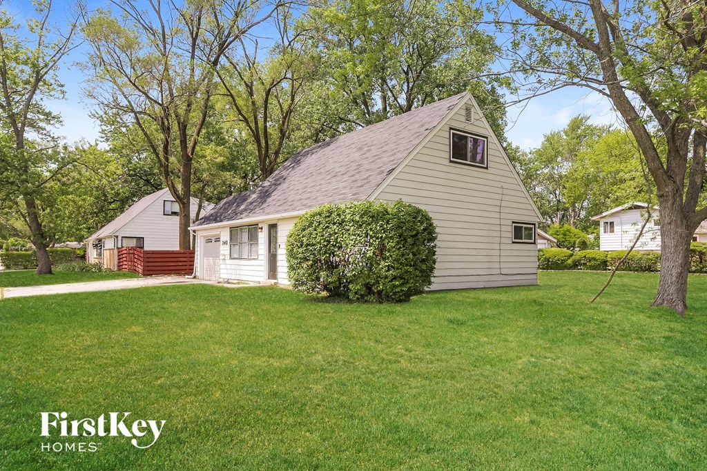 a small white house with a grassy yard and trees