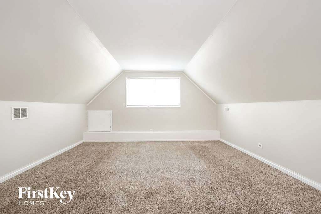 the attic of a home with carpet and a window