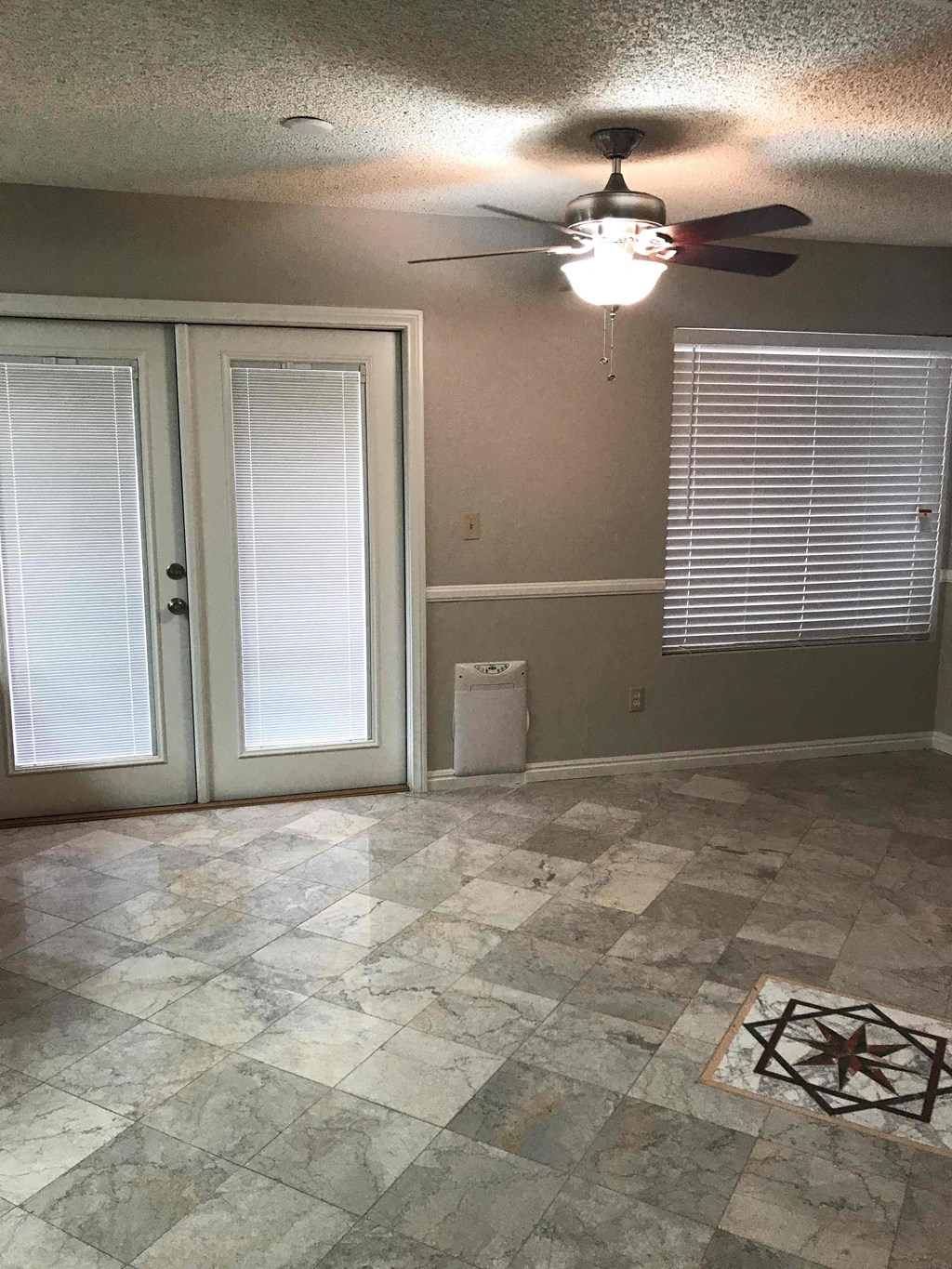 an empty living room with a ceiling fan and glass doors